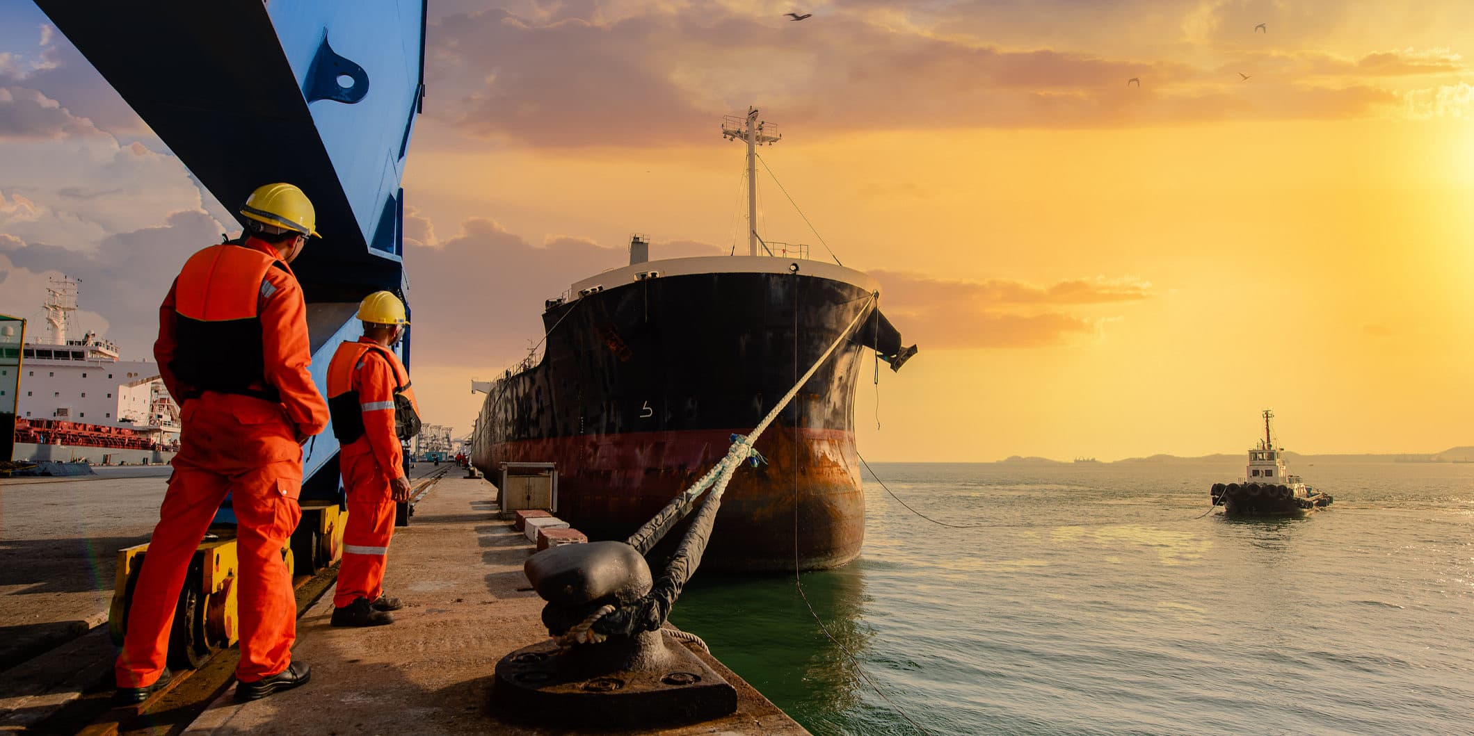 Longshoremen on the dock beside a moored cargo ship at sunset